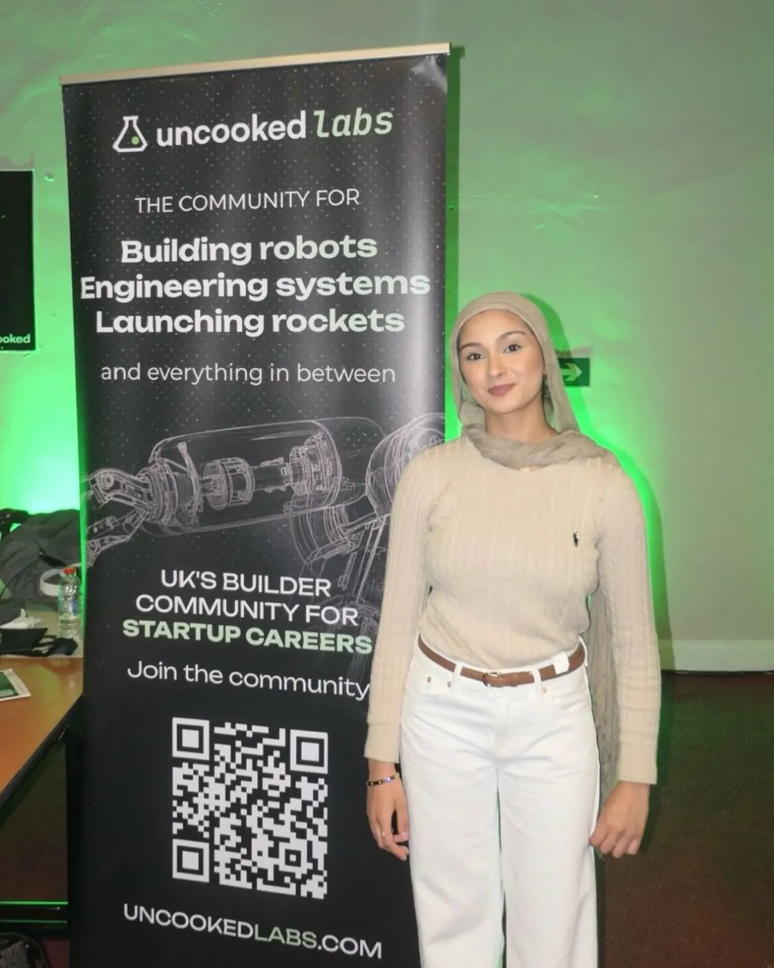 Noor beside the Uncooked Labs banner at Muslim Tech Fest.