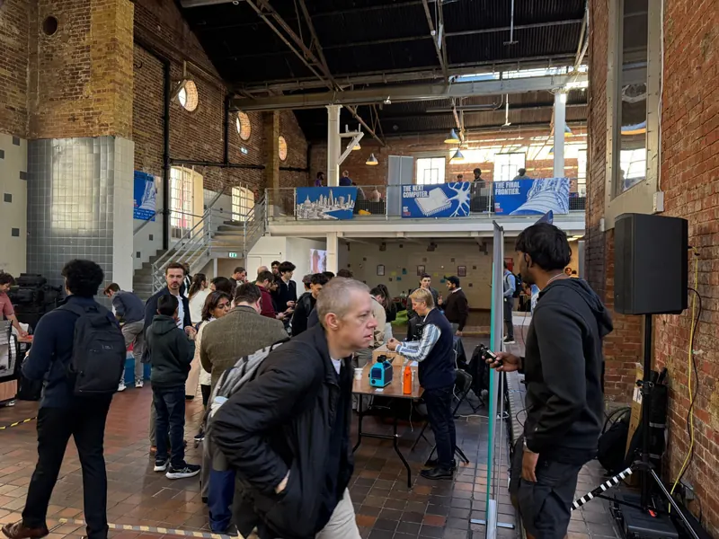 The main hall at Deep Tech London, a brick building with a gallery above hung with banners reading "The next computer." and "The final frontier.", and a crowd of visitors standing and talking on the tiled floor below.