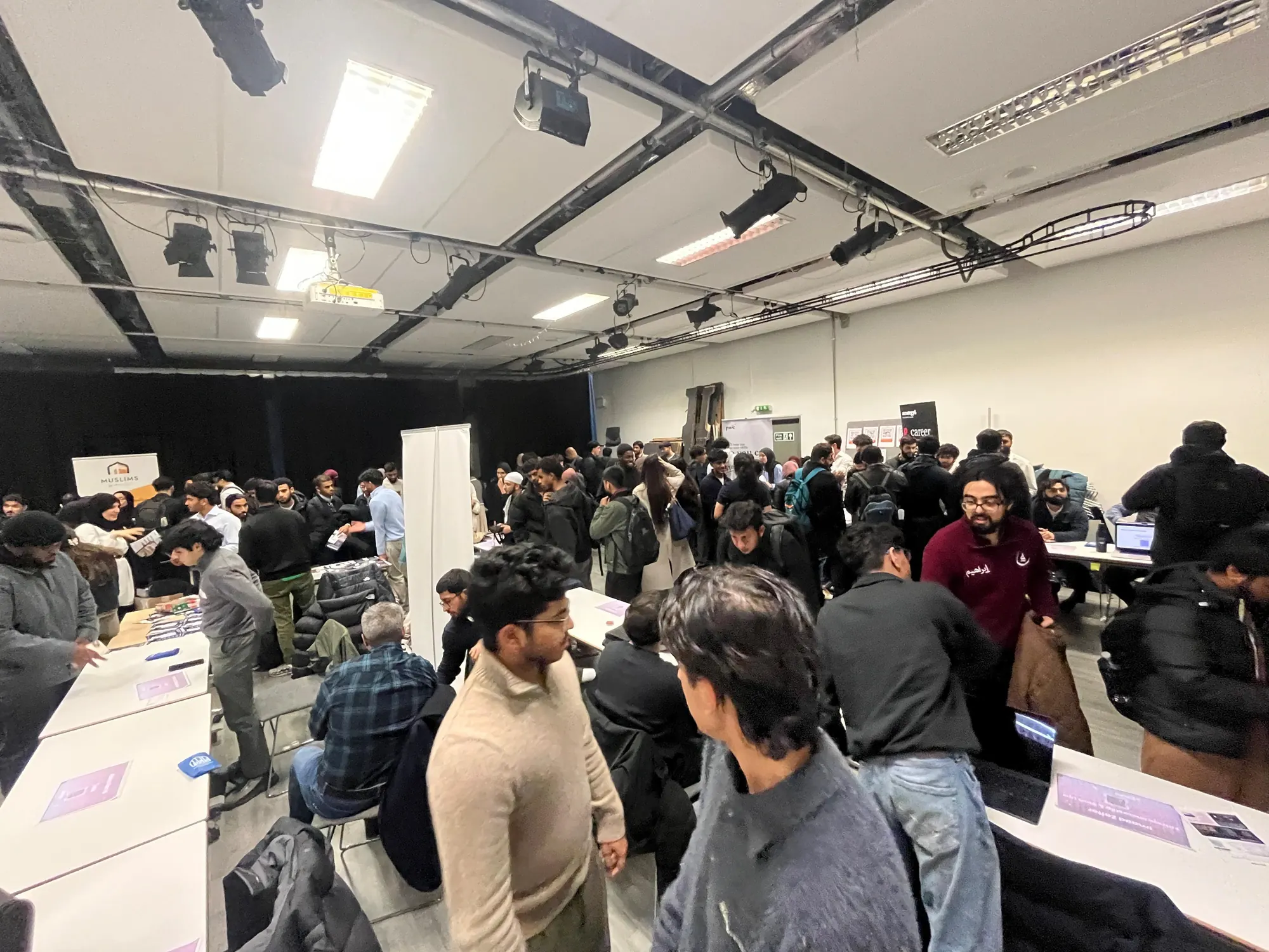 A busy careers fair room at UCL, with students in conversation around tables.