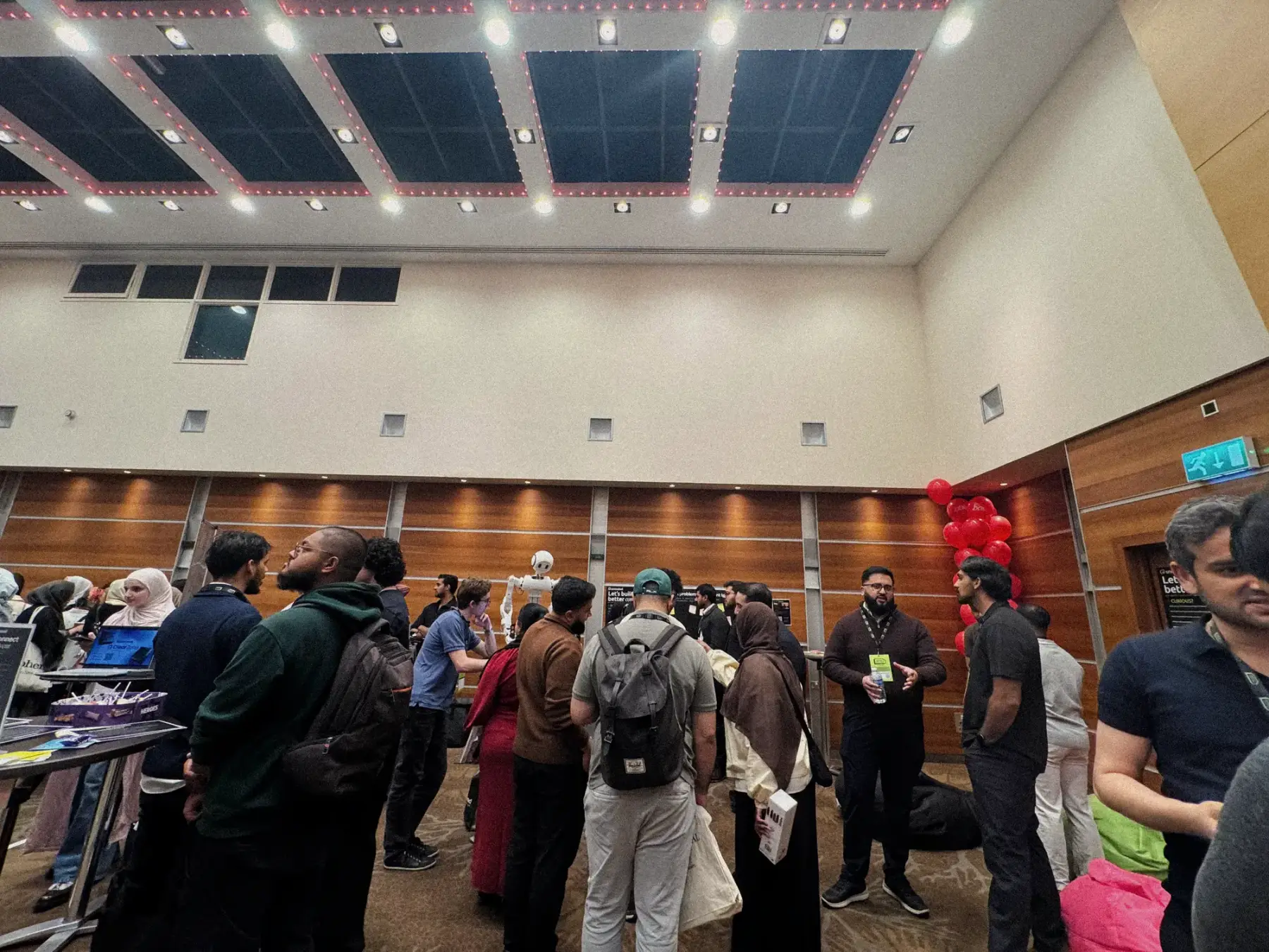 A wide view of a crowded room at MTF, with visitors standing in groups between tables under a dark ceiling.