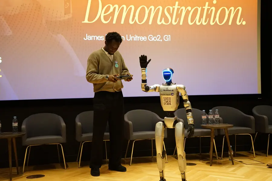 A man holding a controller beside a waving humanoid robot.