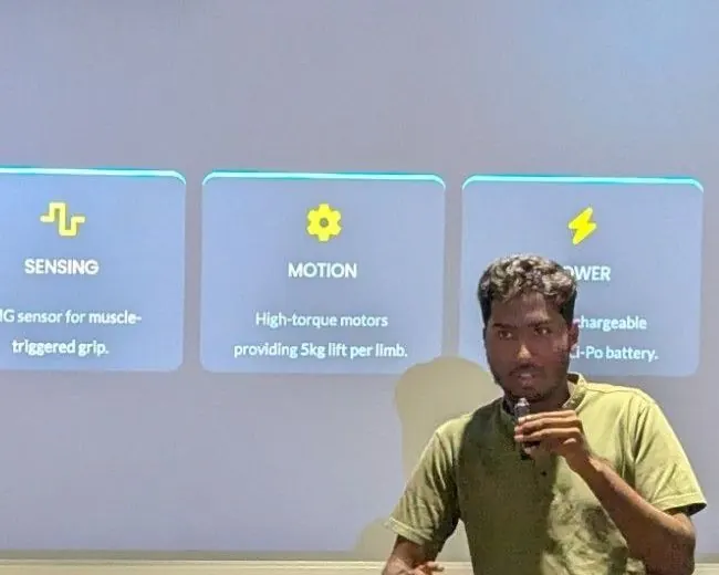 Afiyah Prosthetics pitching their prosthetic arm at the STEMM Haqqathon: the speaker, with a microphone, in front of a slide on the arm's architecture (logic, sensing, motion, power).